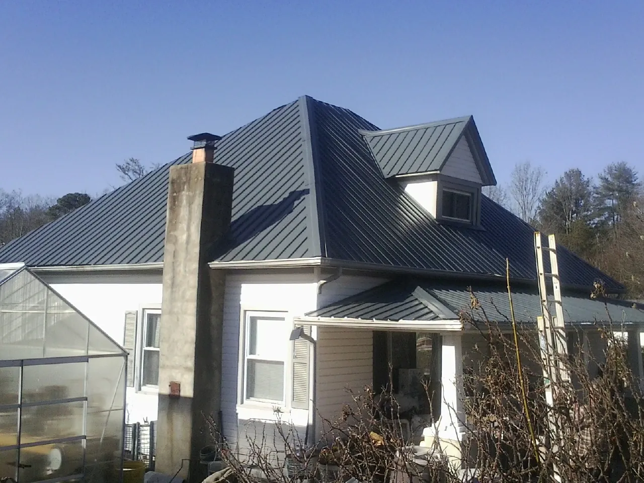 Dark blue standing seam metal roof on a white farmhouse with dormer — Slate & Tile Roof Repair by Roofing Brothers in Benedict