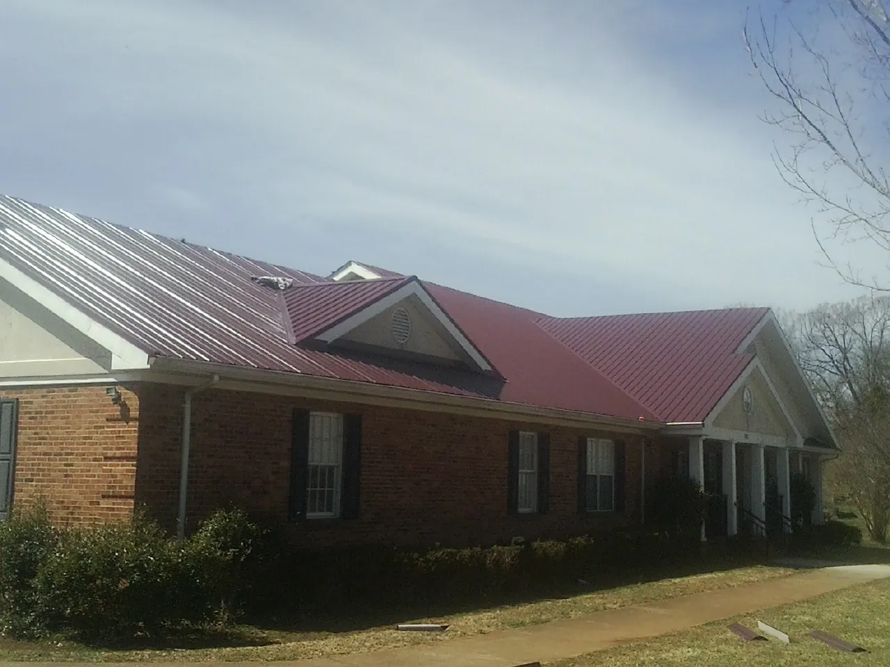 Red metal roof with gabled entries on a long brick building, from a Hail Damage Roof Repair job in Benedict