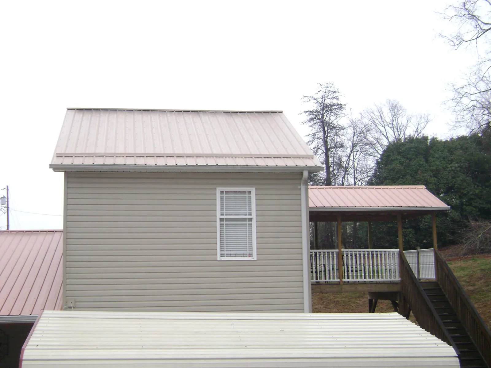 Tan metal roofs on a two story addition and attached porch, from a Roof Replacement job in Benedict